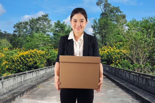 A young woman carrying a box wtih smiling in nature background