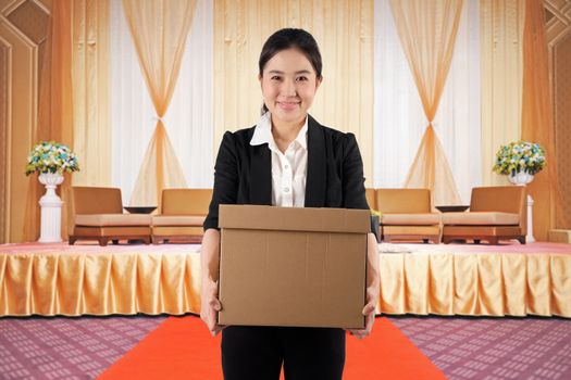 A young woman carrying a box wtih smile in a conference hall