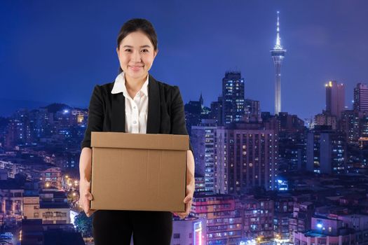 A young woman carrying a box wtih smile in night cityscape background

