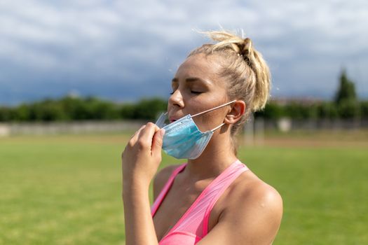 Woman takes off facemask after training or running on sports field. Female breathes deeply