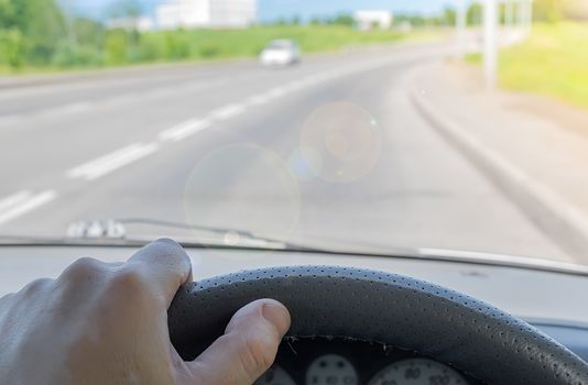 driver hand on the steering wheel of a car that is passing on a country highway