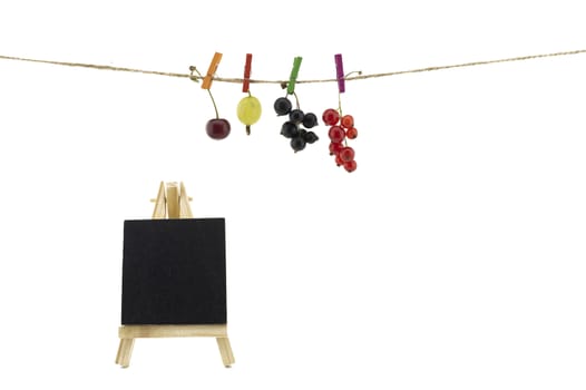 Fresh fruit hanging from clothes pegs on a rope with a fresh cherry, gooseberry, red and black currants and slate chalkboard isolated on white with copy space