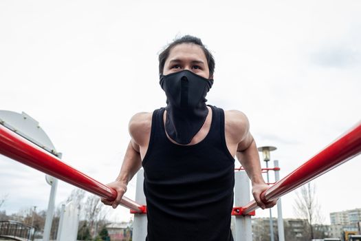 The guy is pushing up on the bars, in a black T-shirt and mask, in quarantine