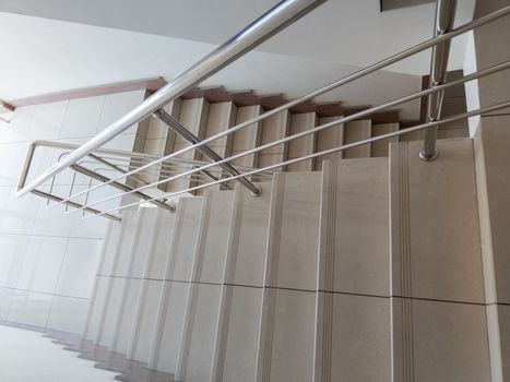 modern design of stanless steel pipes handrail and ceramic tiles staircase in abstract public building, wide angle picture