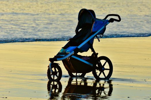 A baby carriage left on a beach; sea waves touching the wheels.
