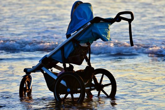 A baby carriage left on a beach; sea waves touching the wheels.