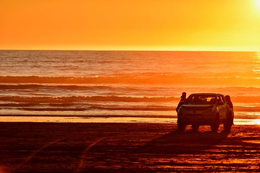 Unidentified people enjoying sunset on a beach.