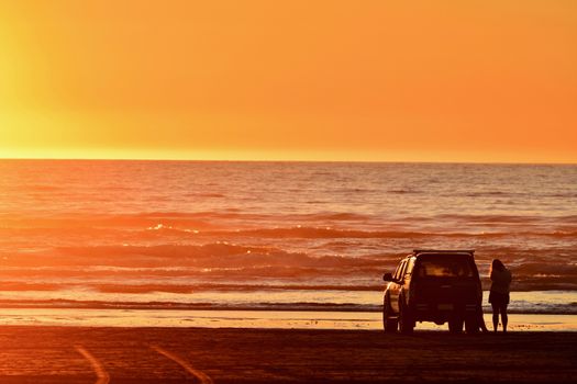 Unidentified people enjoying sunset on a beach.