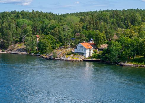 Photo of a white house with a red roof surrounded by green trees on an island in the Swedish archipelago.