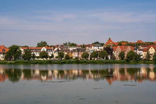 Lakefront houses in Schwerin Germany are reflected in the waters of the lake on a summer morning.
