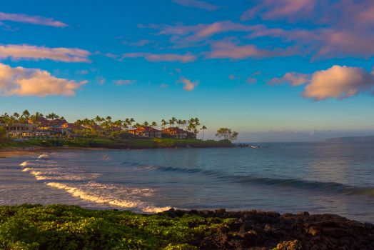 The golden sun of late afternoon lights a beach in Maui Hawaii as waves roll gently in to shore.