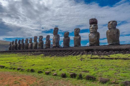 Wide angle shot of 15 Moai statues facing inward over Easter Island at Tongariki with a dramatic white cloud and blue sky background.