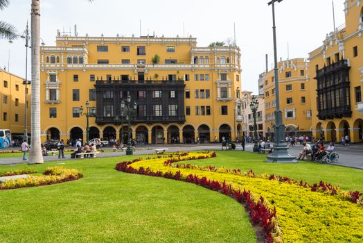 Tourists, residents and shoppers in the center of Lima Peru, the Plaza Mayor, with its flowers and yellow buildings.