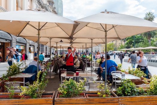 Santiago, Chile--April 6, 2018. Diners enjoy lunch at an outdoor cafe on the boulevard in Santiago, Chile; A waiter signals an open table for 2 more c