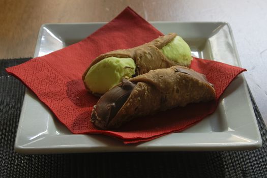 Two cannolis with chocolate and pistachio filling served on a white dish with a red napkin.