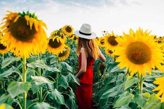 woman in red dress and hat entering sunflower field