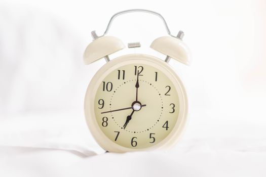 Alarm clock on wooden table for wake up time with light from window, selective focus