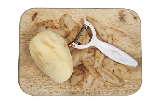 Raw potato peeled on a wooden chopping board with peeler cut out and isolated on a white background