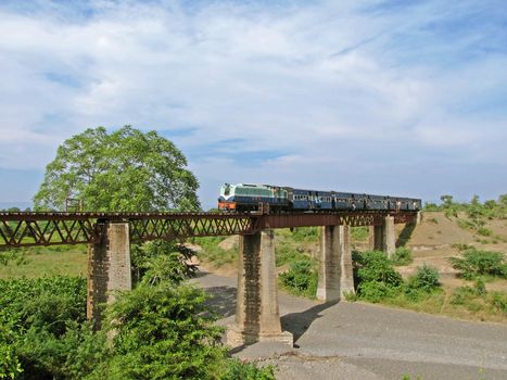 A small  narrow gauge train with diesel locomotive crossing an old stone and iron  bridge in Chamak, Maharashtra, India.