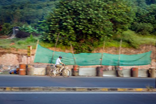 Pune, Maharashtra, India - October 4th, 2017 : Motion blur image of an old bicycle rider wearing helmet for safety on a way for fitness.
