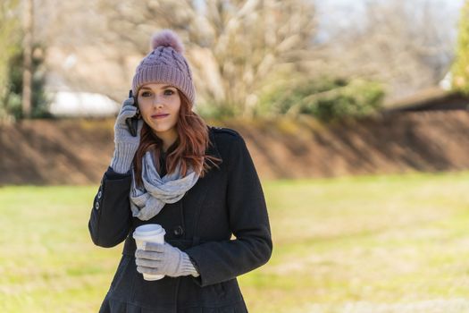 A gorgeous blonde model enjoys a winters day outdoors while drinking her favorite drink and talking on her cellphone