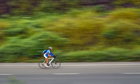 Motion blur, panning image of an isolated  bicycle rider wearing helmet for safety on a way for fitness.