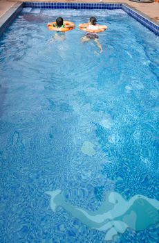 The mother and child are swimming in the resort's pool to have fun. With life jackets worn for safety and protection against drowning.