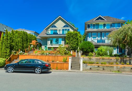 Suburban family houses with landscaped terraces a car parked in front on blue sky background