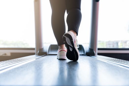 Close up female feet wearing sneakers running on treadmill at fitness gym. Diet lifestyle, weight loss, stomach muscle, healthy concept.