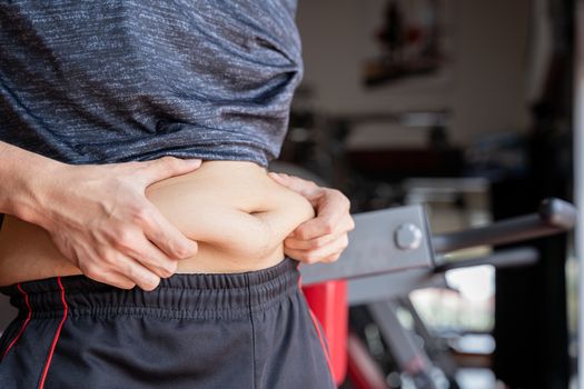 Fat man holding excessive fat belly, overweight fatty belly at fitness gym. Diet lifestyle, weight loss, stomach muscle, healthy concept.