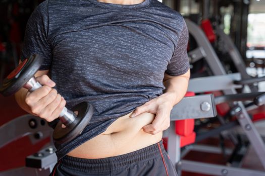 Fat man holding dumbbell and excessive fat belly, overweight fatty belly at fitness gym. Diet lifestyle, weight loss, stomach muscle, healthy concept.