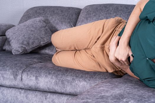 Young man suffering from abdominal pain while lying on sofa at home. Healthcare medical or daily life concept.
