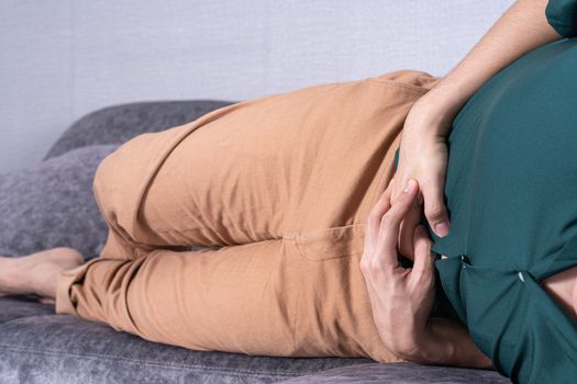 Young man suffering from abdominal pain while lying on sofa at home. Healthcare medical or daily life concept.