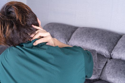 Young man suffering from neck pain while sitting on sofa at home. Healthcare medical or daily life concept.