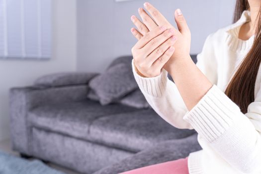 Young woman suffering from hand pain while sitting on sofa at home. Healthcare medical or daily life concept.