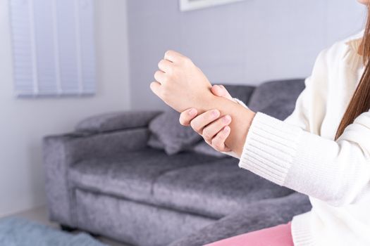 Young woman suffering from wrist pain while sitting on sofa at home. Healthcare medical or daily life concept.