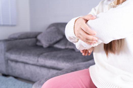 Young woman suffering from elbow pain while sitting on sofa at home. Healthcare medical or daily life concept.