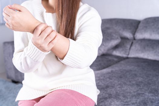 Young woman suffering from wrist pain while sitting on sofa at home. Healthcare medical or daily life concept.