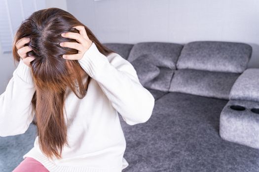 Young woman suffering from head pain while sitting on sofa at home. Healthcare medical or daily life concept.