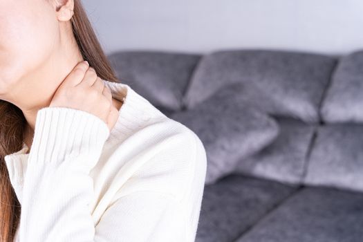 Young woman suffering from neck pain while sitting on sofa at home. Healthcare medical or daily life concept.