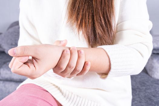 Young woman suffering from wrist pain while sitting on sofa at home. Healthcare medical or daily life concept.