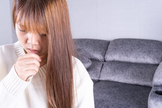 Asian beautiful woman coughing while sitting on sofa at home. Healthcare medical or daily life concept.
