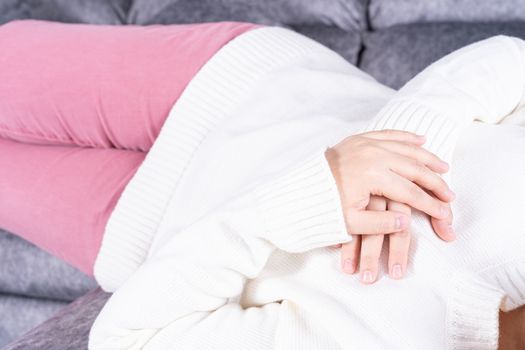 Young woman suffering from heart pain while sitting on sofa at home. Healthcare medical or daily life concept.