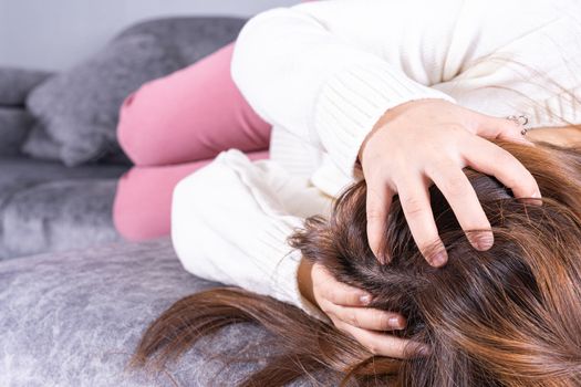 Young woman suffering from head pain while sitting on sofa at home. Healthcare medical or daily life concept.