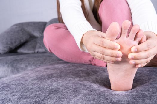 Young woman suffering from foot pain while sitting on sofa at home. Healthcare medical or daily life concept.