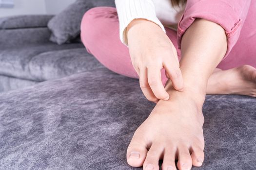 Young woman scratching his foot while sitting on sofa at home. Healthcare medical or daily life concept.