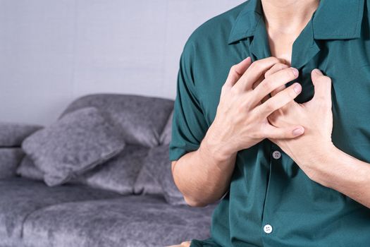 Young man suffering from heart pain while sitting on sofa at home. Healthcare medical or daily life concept.