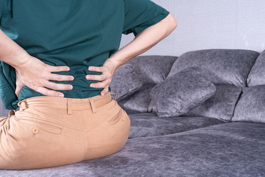 Young man suffering from back pain while sitting on sofa at home. Healthcare medical or daily life concept.