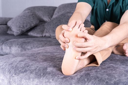 Young man suffering from foot pain while sitting on sofa at home. Healthcare medical or daily life concept.