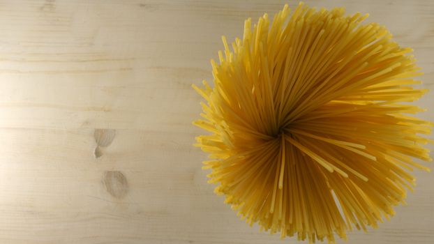 Top down flat lay view of a handful of spaghetti spoked spots that look like a yellow flower on a light wooden table background italian food cuisine copy space